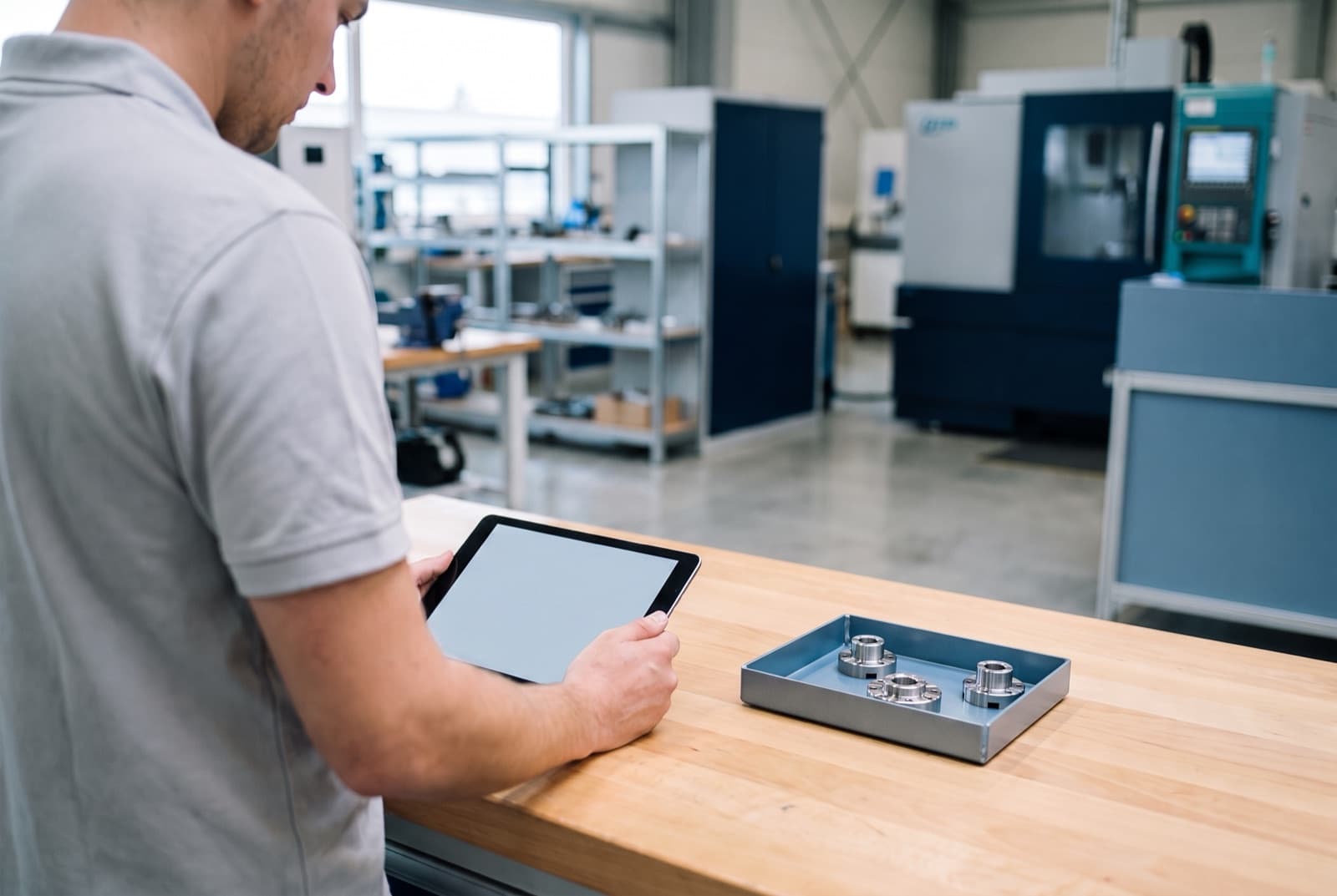Ingénieur qualité examinant des pièces usinées et une tablette sur un établi d'atelier bien rangé