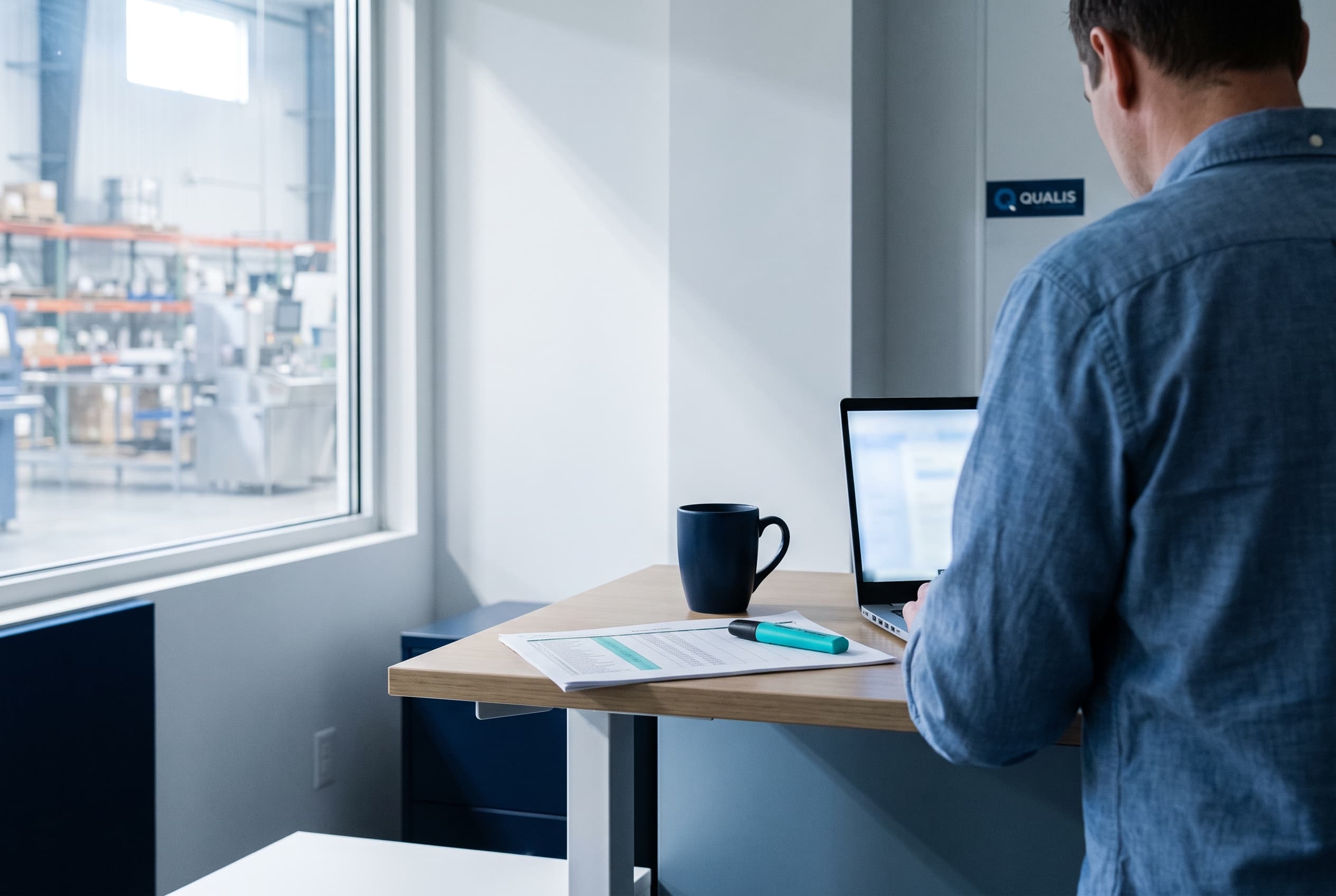 Un responsable des opérations consulte les créances clients sur un ordinateur portable, dans un bureau d'usine lumineux